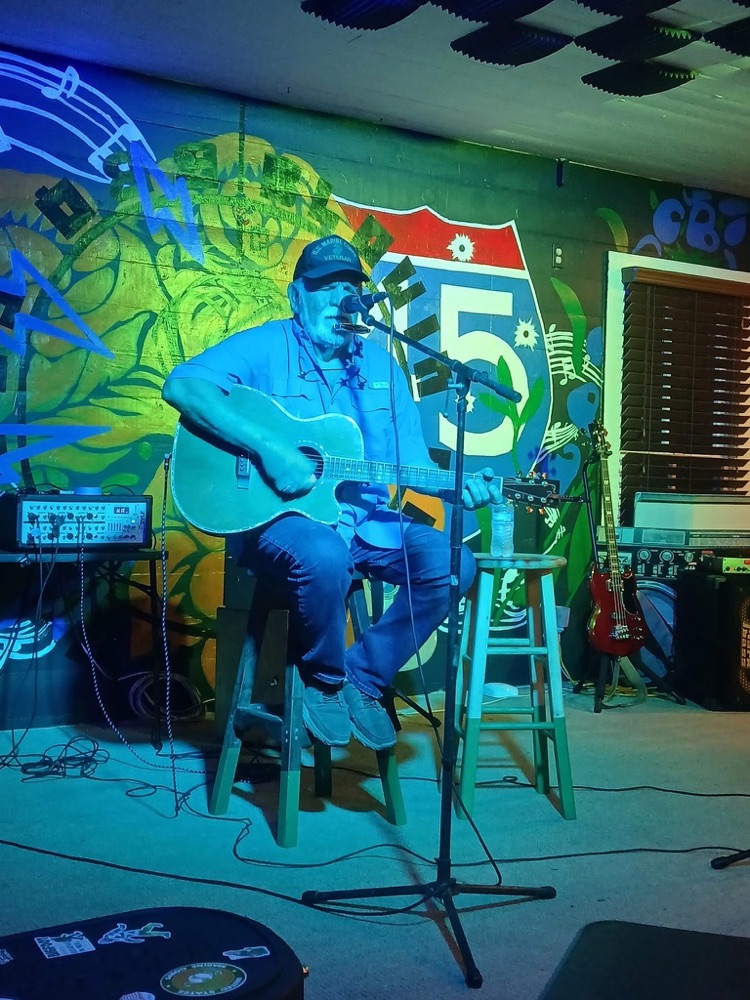 Kokomo Joe playing guitar on stage in front of a mural