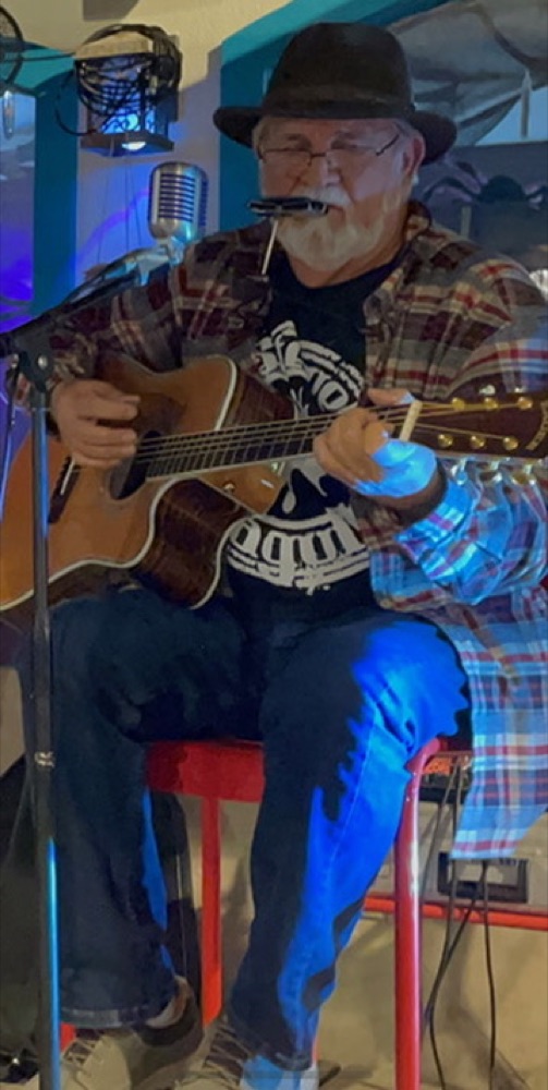 Kokomo Joe playing harmonica and guitar under colorful stage lights
