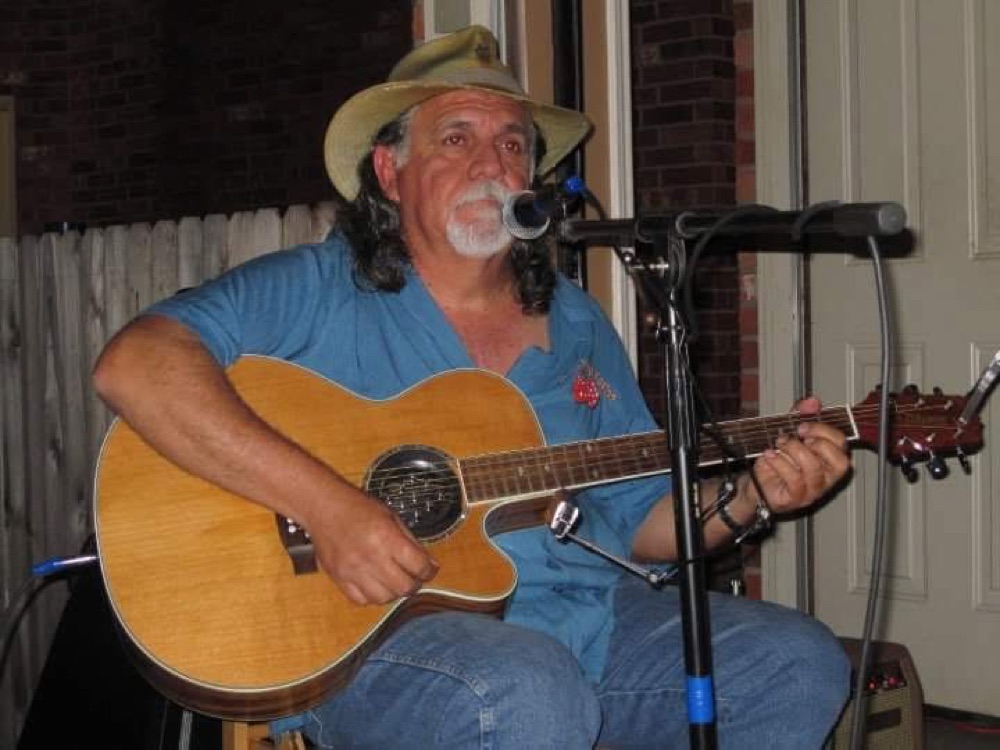 Kokomo Joe singing into a microphone while playing guitar