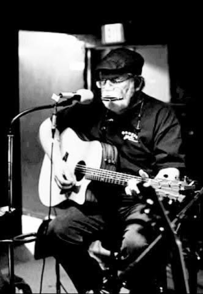 Black and white photo of Kokomo Joe playing harmonica and guitar